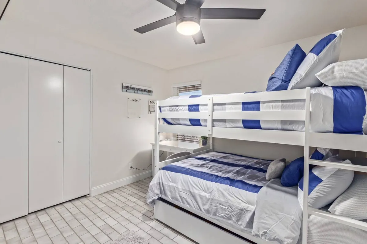 A playful bedroom showcasing a sturdy bunk bed dressed in blue and white bedding, complete with a ceiling fan overhead. The setting feels inviting and fun, suitable for families or groups needing flexible sleeping options.