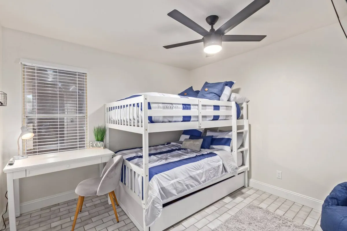 A playful and comfortable bedroom with modern bunk beds, a desk, ceiling fan, and decorative pillows. The space is designed for versatility—accommodating relaxation, sleep, study, or play. Fresh paint and new furniture are evident, reflecting the home's turnkey appeal.
