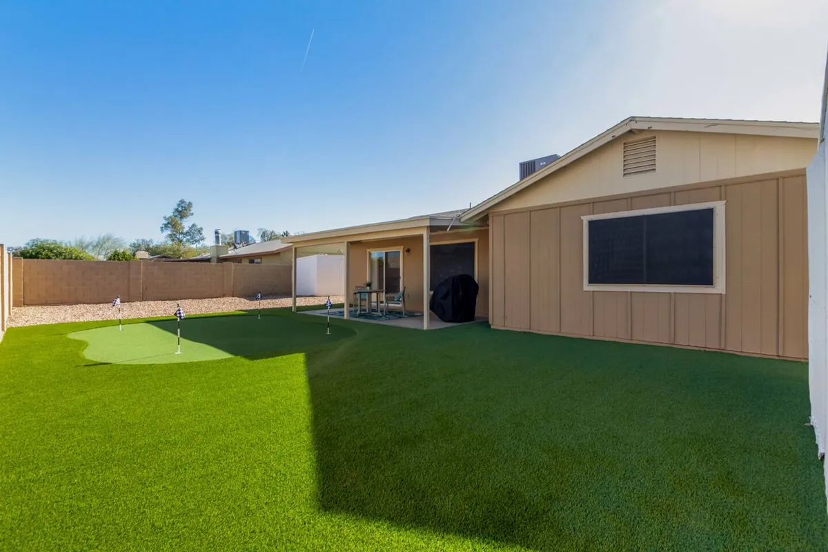 A vibrant backyard scene showcasing a lush green lawn, a dedicated golf putting area, and a stylish patio seating arrangement. The space radiates with natural light and offers multiple options for outdoor relaxation, entertainment, and play.