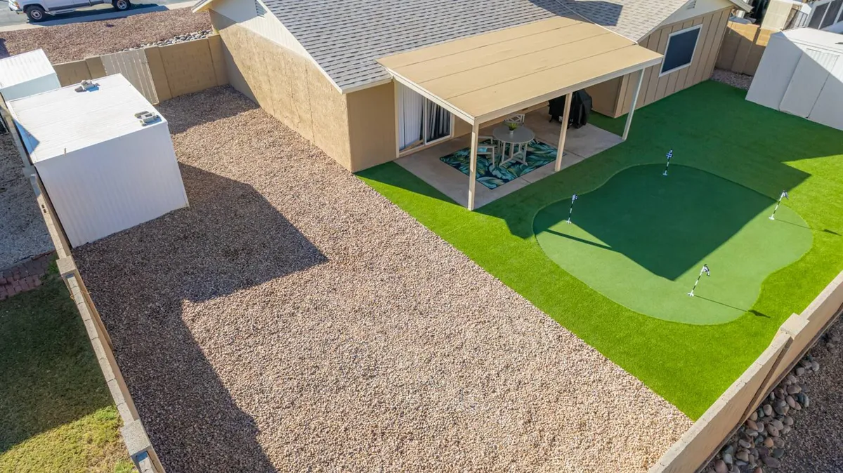 An exterior shot featuring a landscaped backyard with an artificial putting green, covered patio, and gravel landscaping. The scene is leisurely and flexible, suggesting opportunities for both productive breaks and informal networking or relaxation outdoors.