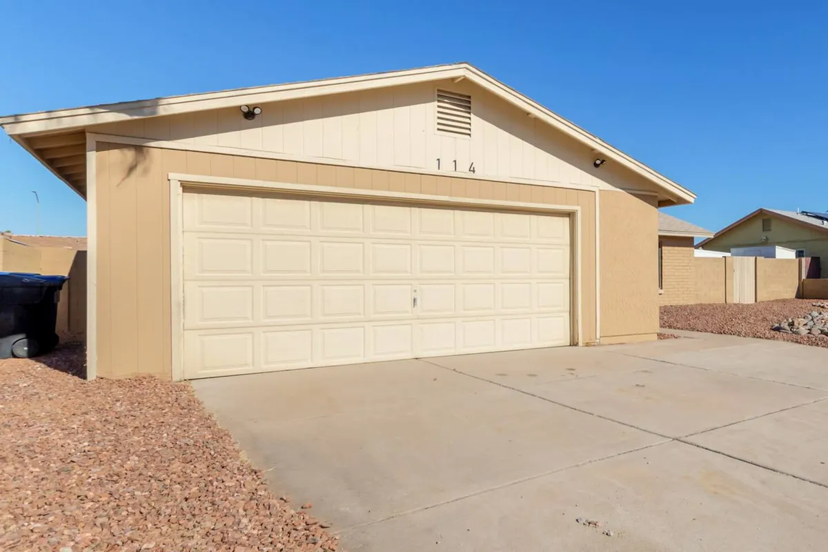 This exterior image shows the home's inviting garage door, clearly visible house number, and well-maintained landscaping rocks along the driveway. The scene evokes a sense of a welcoming, calm residential neighborhood, perfect for business travelers seeking both comfort and professionalism.