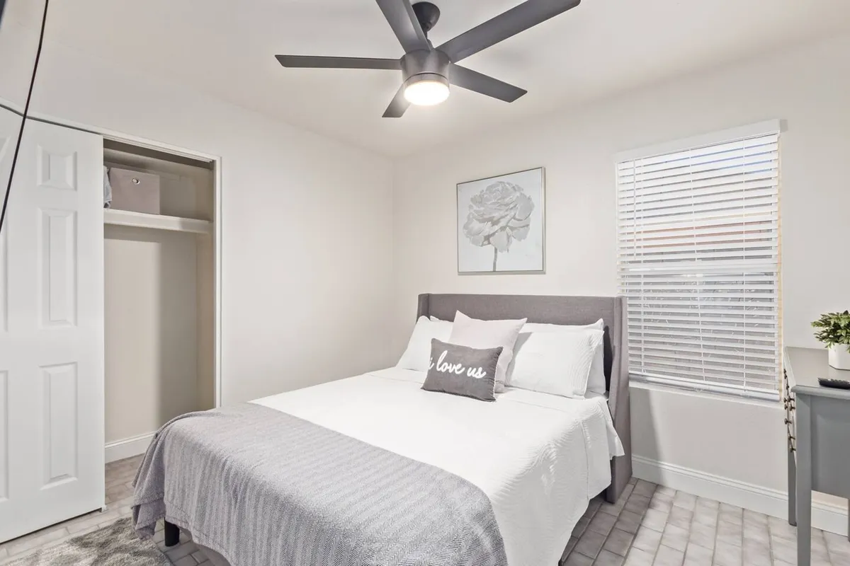 A serene bedroom featuring a plush bed topped with soft bedding, stylish wall art above the headboard, and a nightstand with a lamp. The space is filled with natural light, creating a calm and cozy atmosphere ideal for relaxation and restful nights.