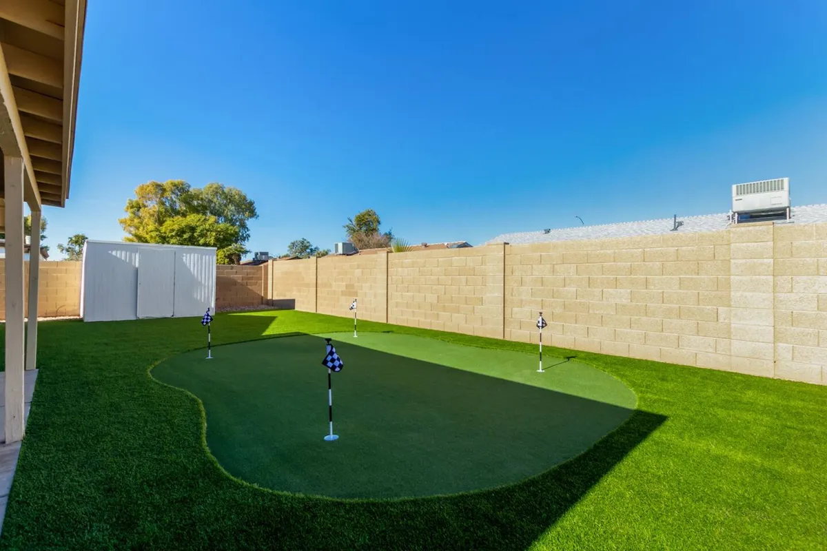 This exterior scene features a lush putting green complete with golf flags, framed by boundary walls and surrounded by well-maintained landscaping. It evokes a playful, relaxed vibe and hints at activities like golf practice, family gatherings, and outdoor relaxation.